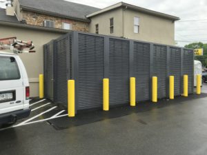 PalmSHIELD's horizontal louvered enclosure in a dark gray surrounds one said of Mission Dispensary and contrasts pleasingly with some bright yellow traffic columns to increase protection